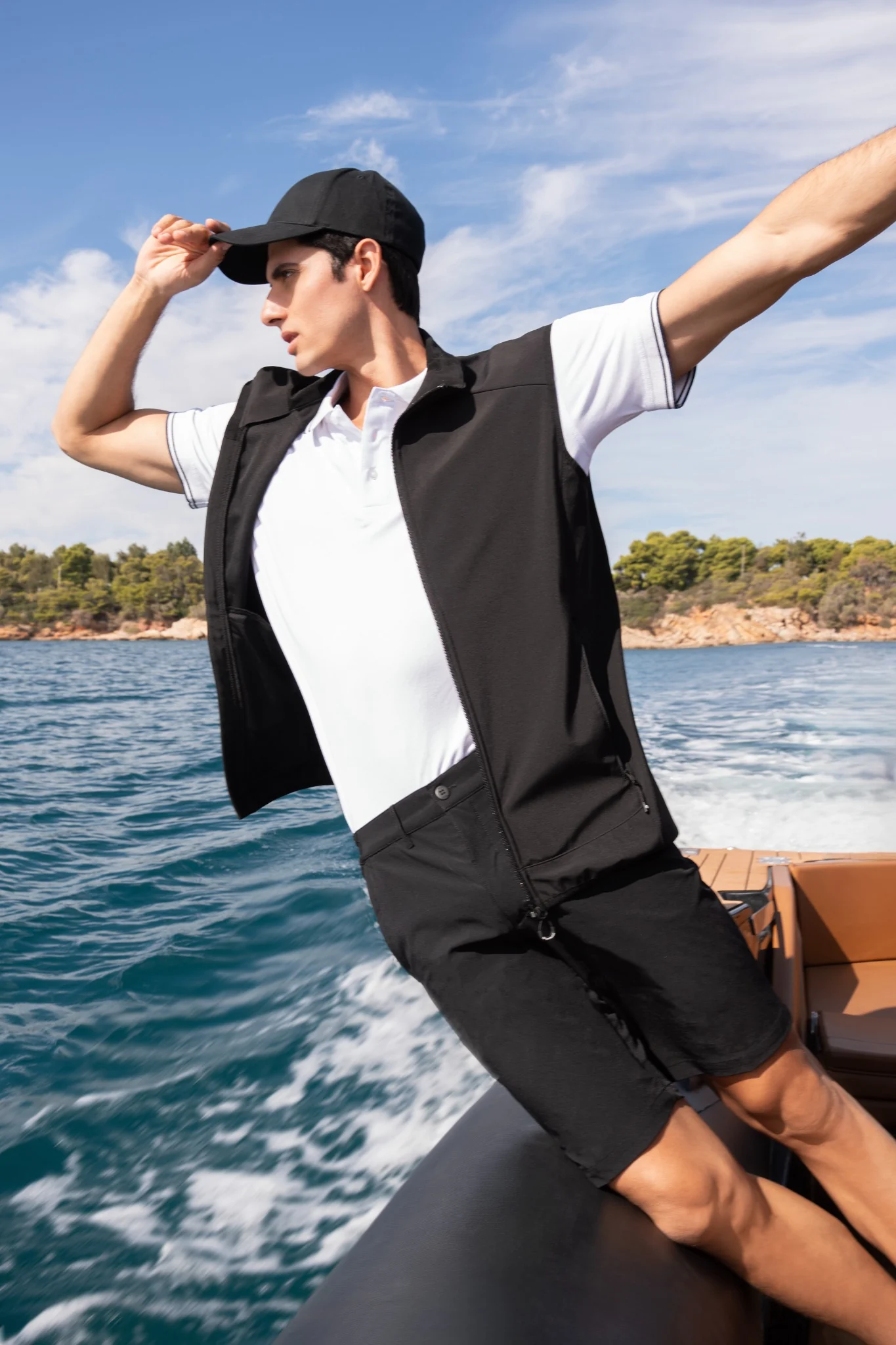 Male model in a black vest and white polo aboard a moving tender