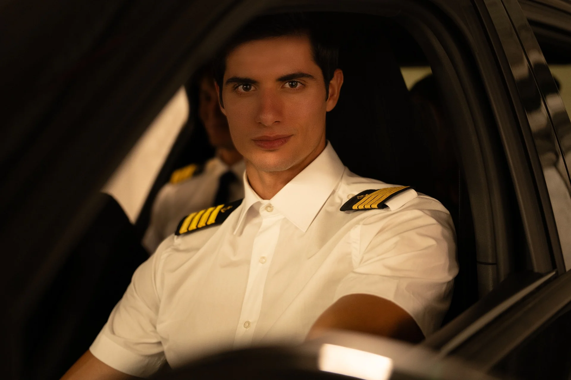 Portrait of a male model in a white captain’s shirt, seated in a car