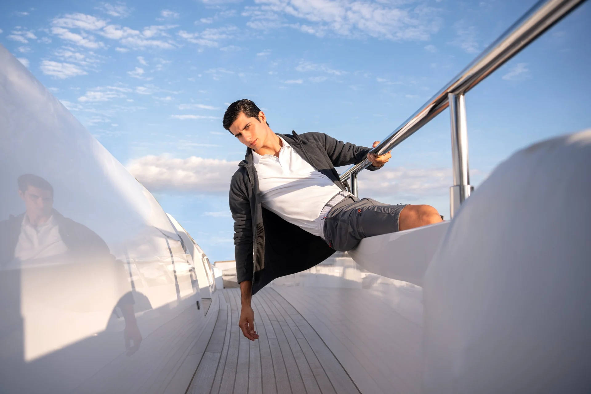 Male model seated on yacht steps beneath a blue sky
