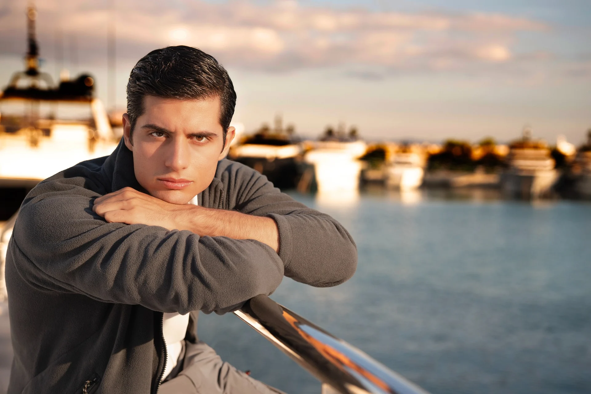 Close portrait of a male model leaning on a yacht railing at golden hour