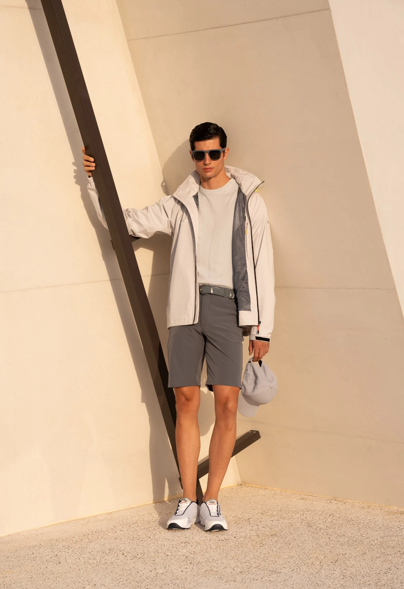 Male model in a light jacket and grey shorts against a warm architectural backdrop