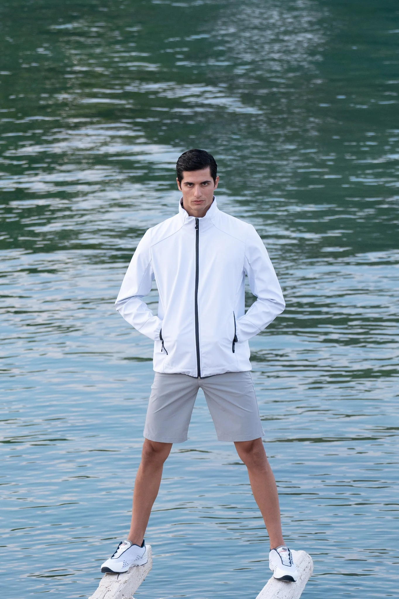 Male model in a white jacket standing above the water at the marina