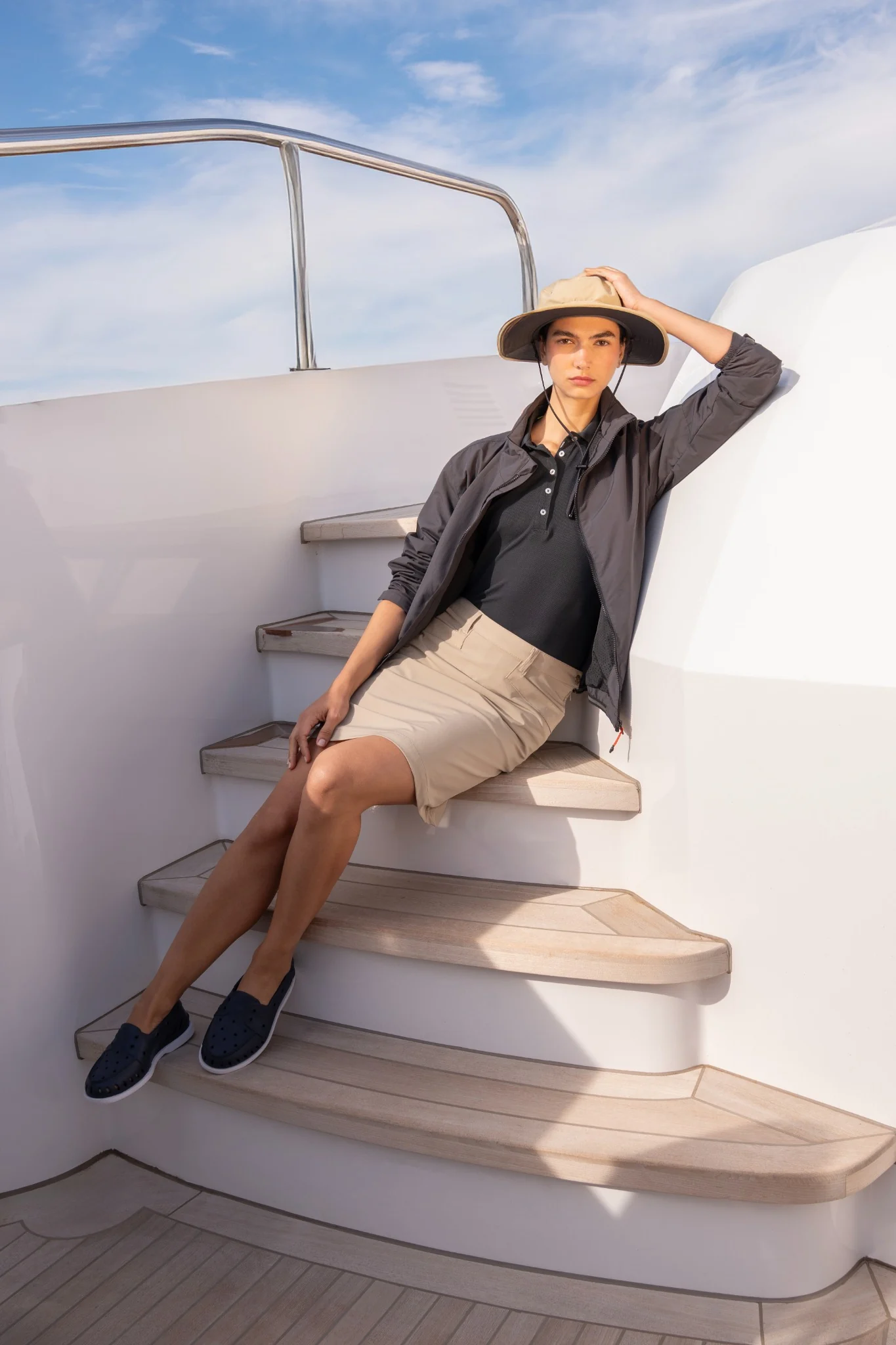 Female model wearing a sun hat, seated on the curved steps of a yacht