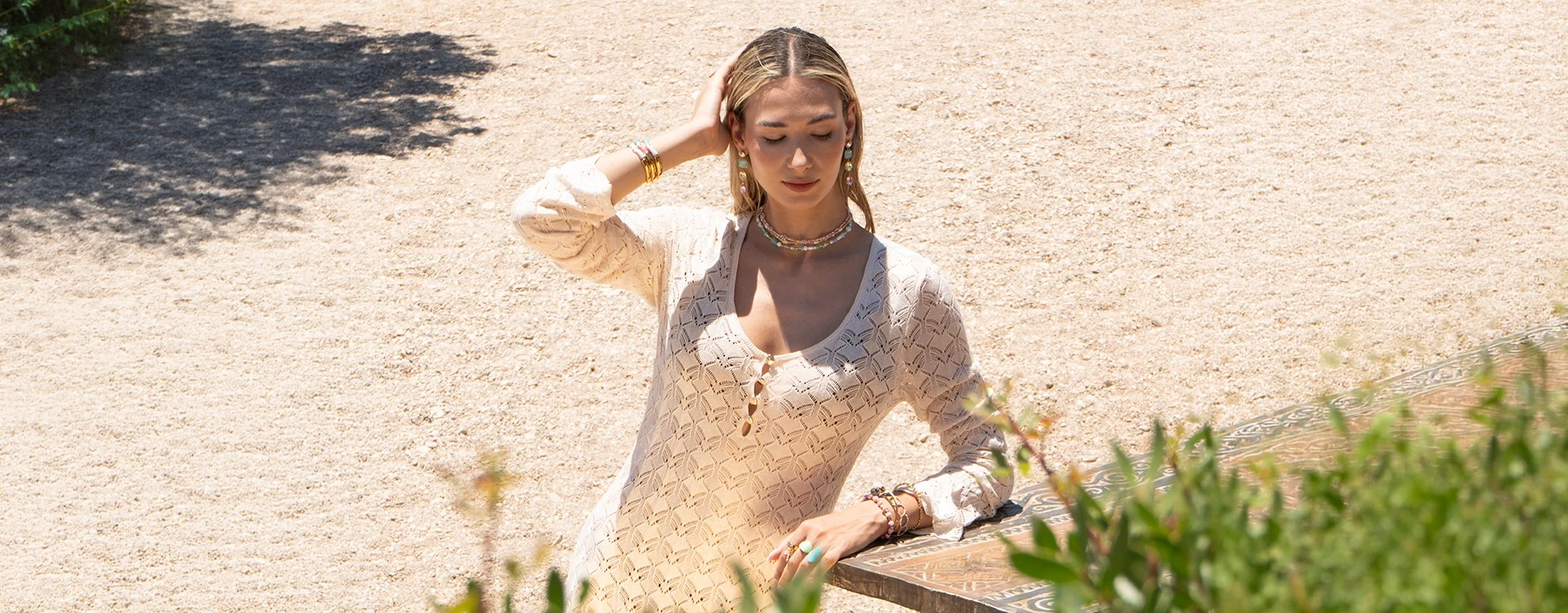 Wide view of a model in a white crochet dress beside beach bar greenery
