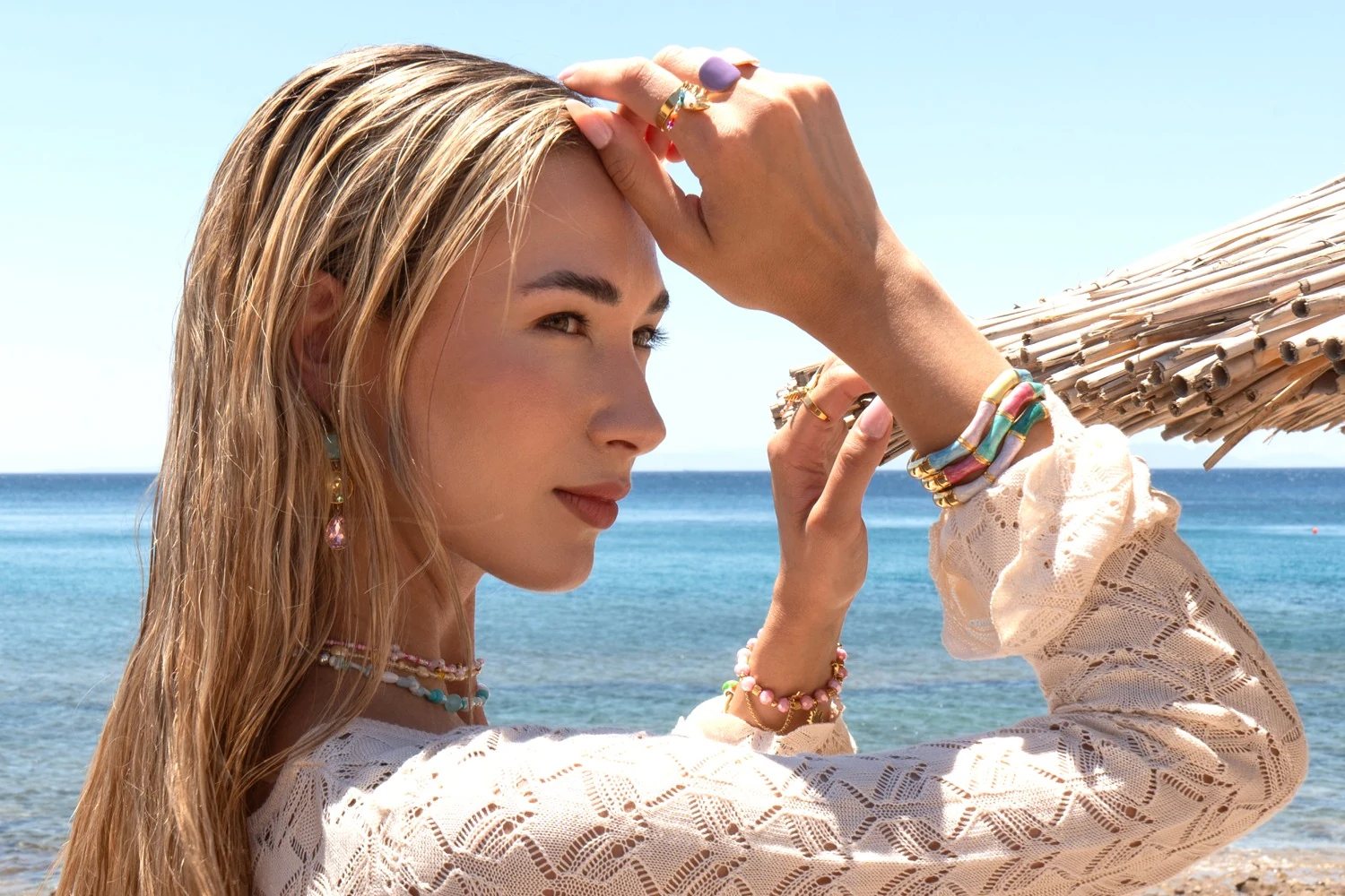 Seaside portrait with colourful jewellery and a white crochet top against the blue sea