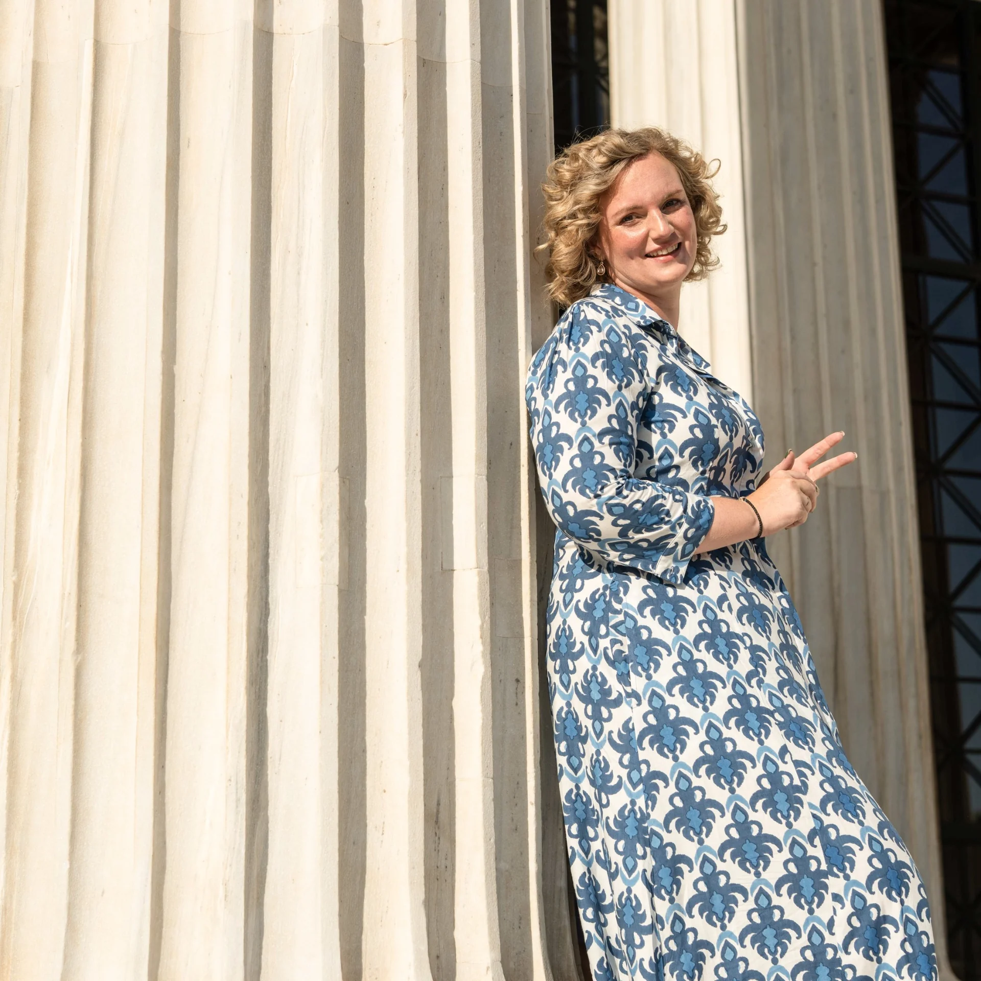 Melina standing beside a carved column in a blue patterned dress