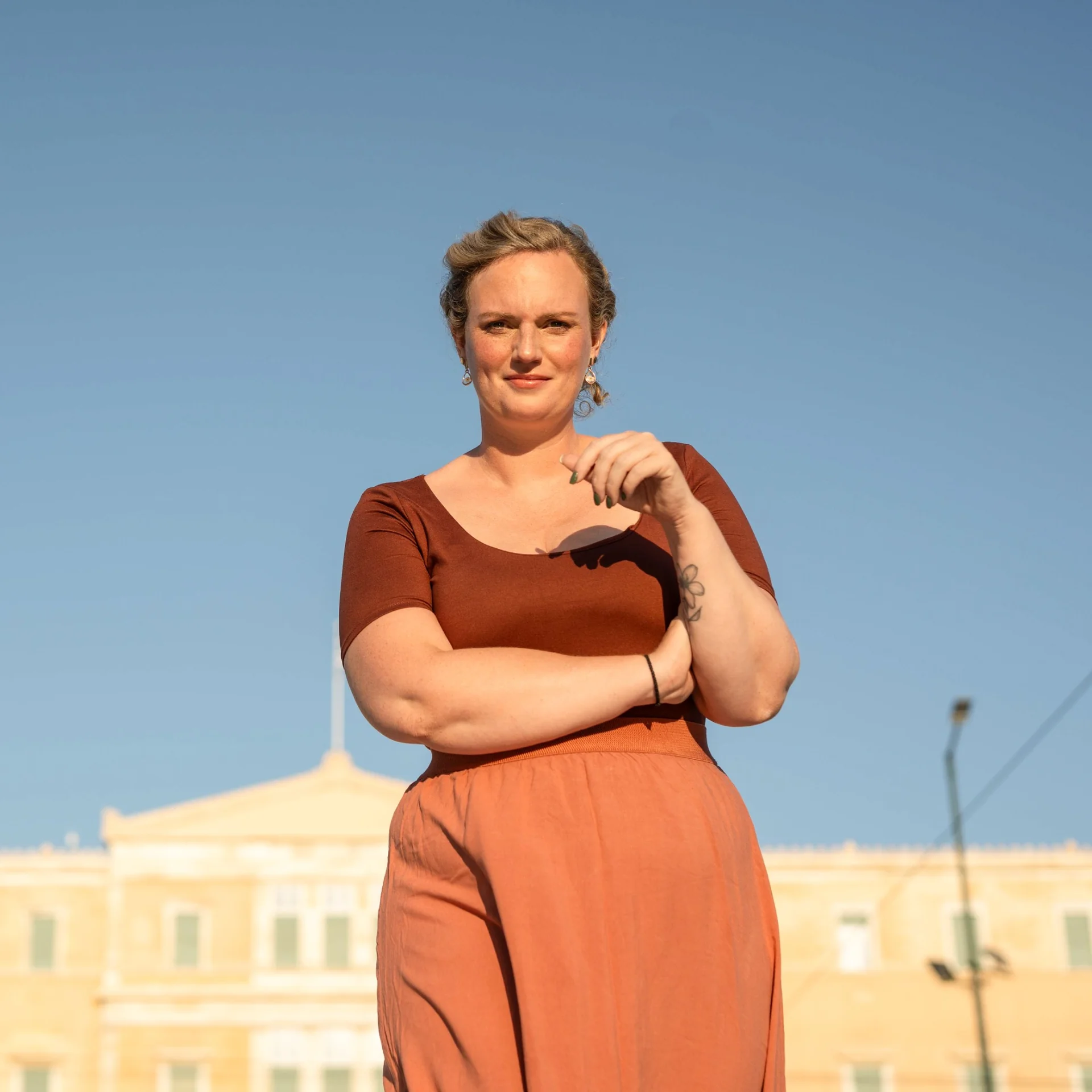 Melina in terracotta tones beneath a clear blue Athens sky
