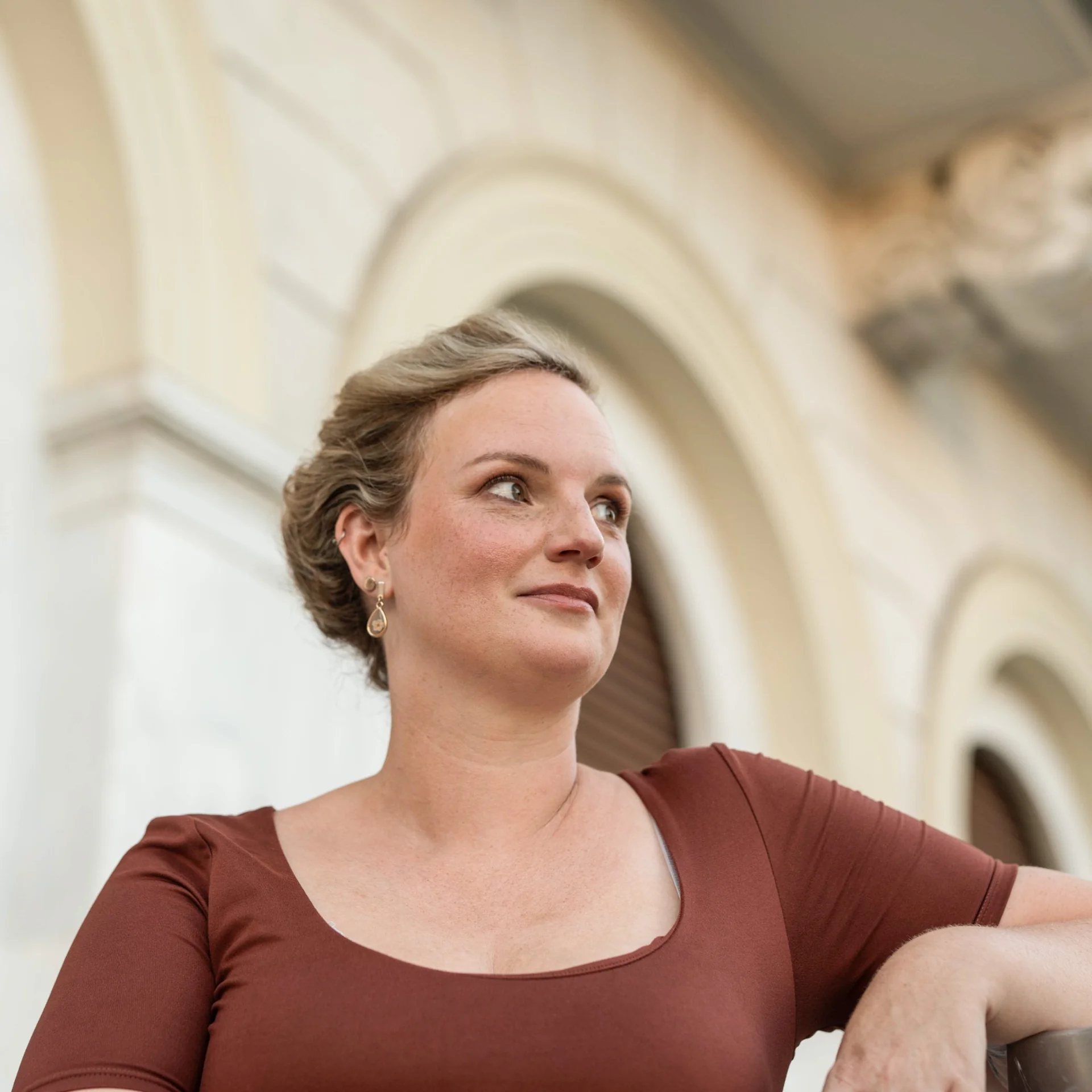 Melina looking to one side against softly focused pale architecture