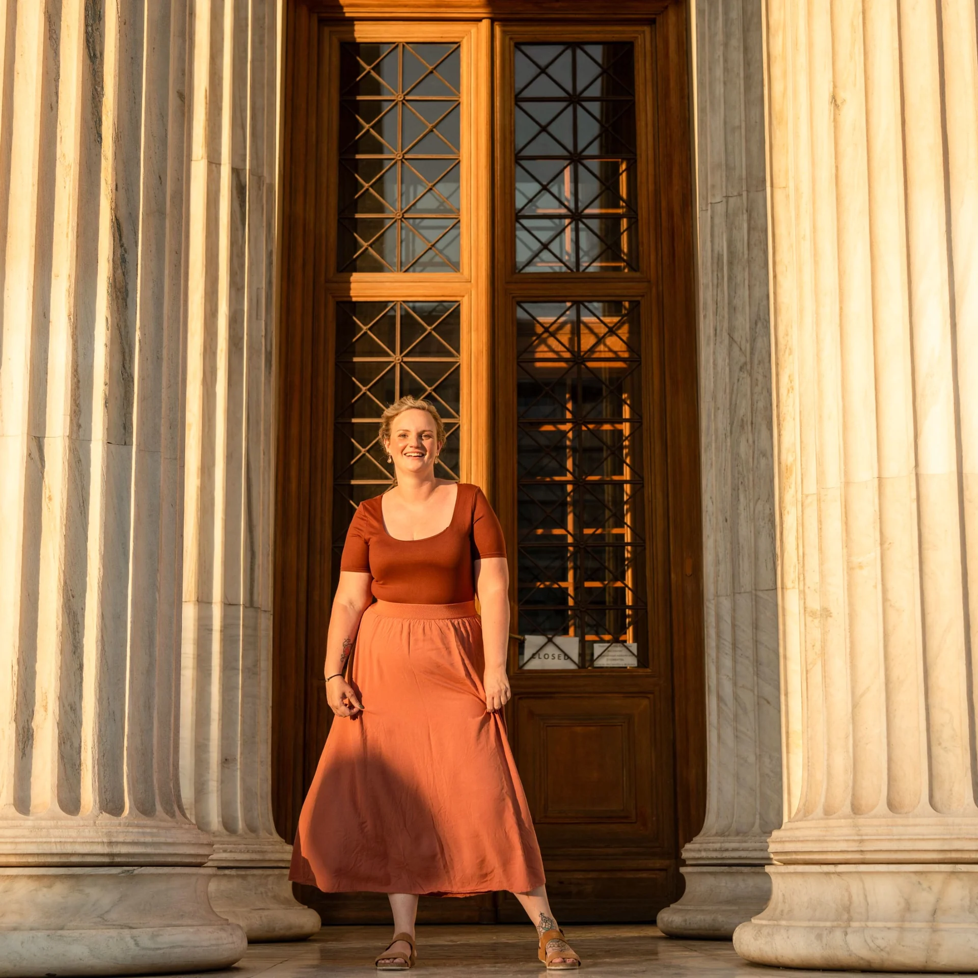 Full-length portrait of Melina framed by classical columns and a tall doorway