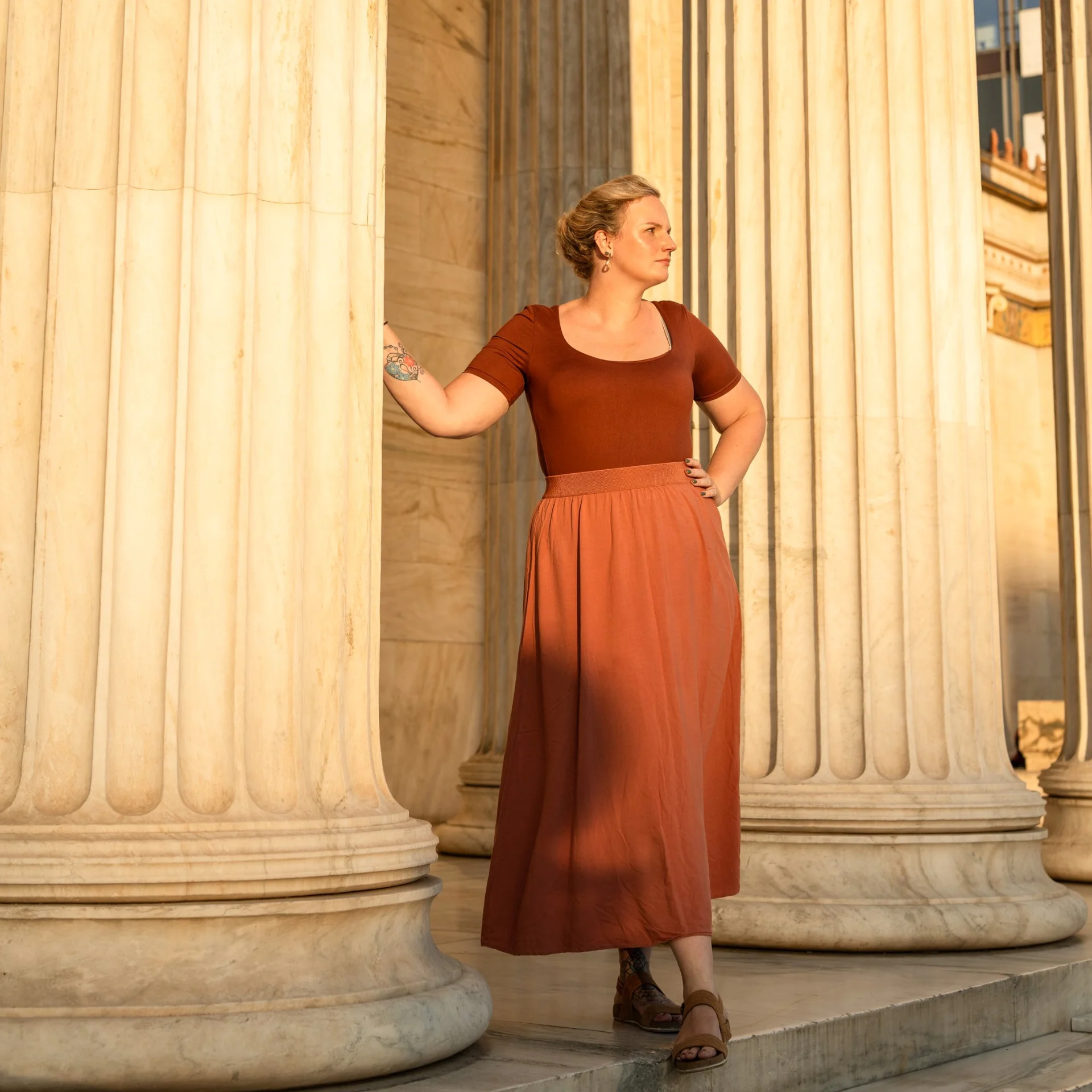 Melina in a terracotta skirt standing between warm stone columns