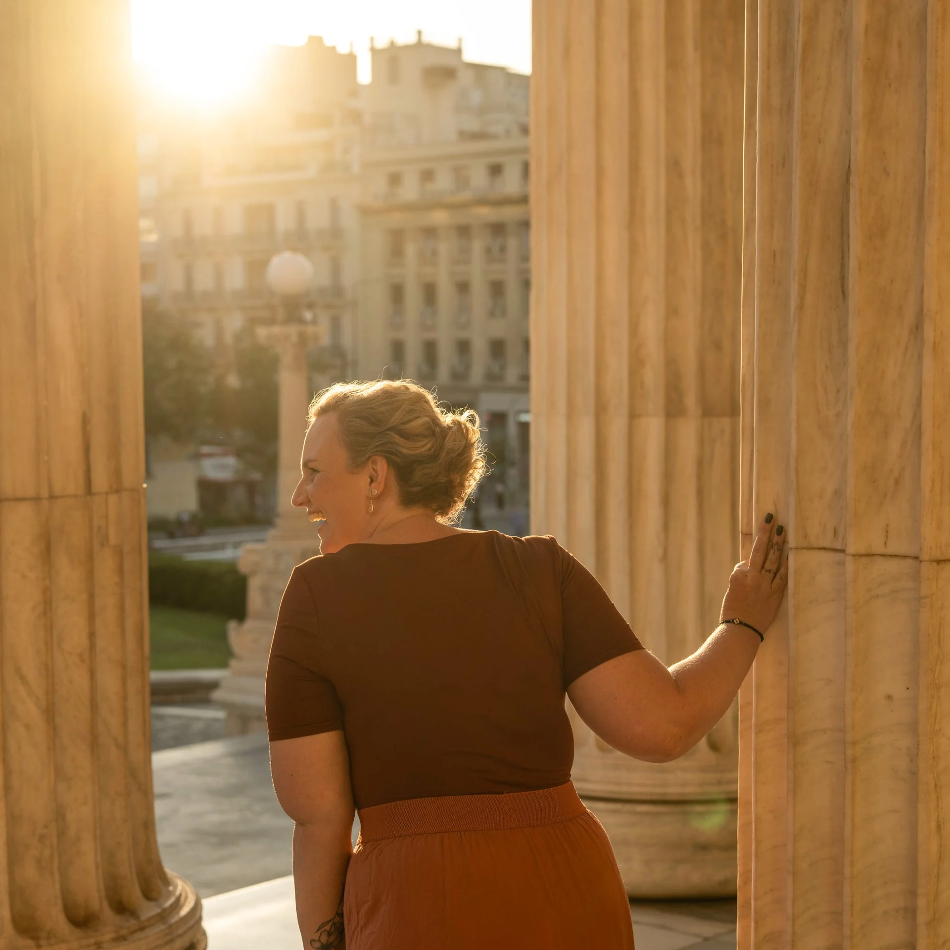 Melina turning towards golden sunlight between stone columns
