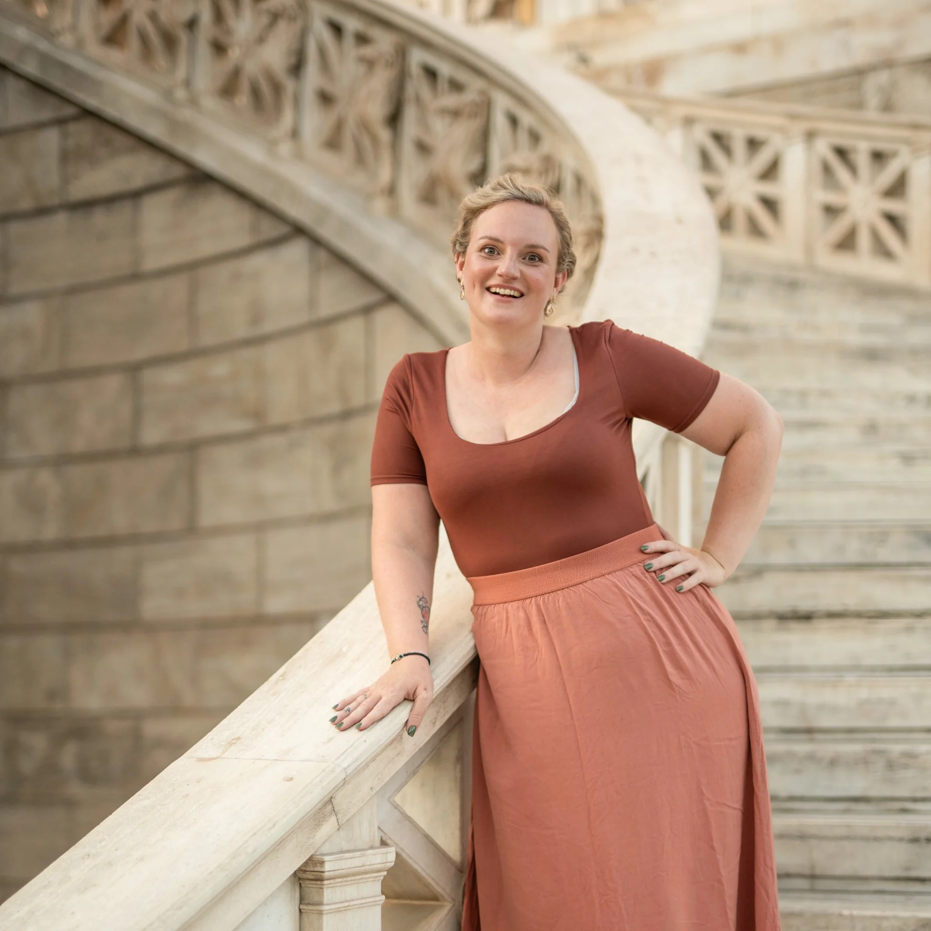 Melina smiling beside a stone stairway and carved balustrade
