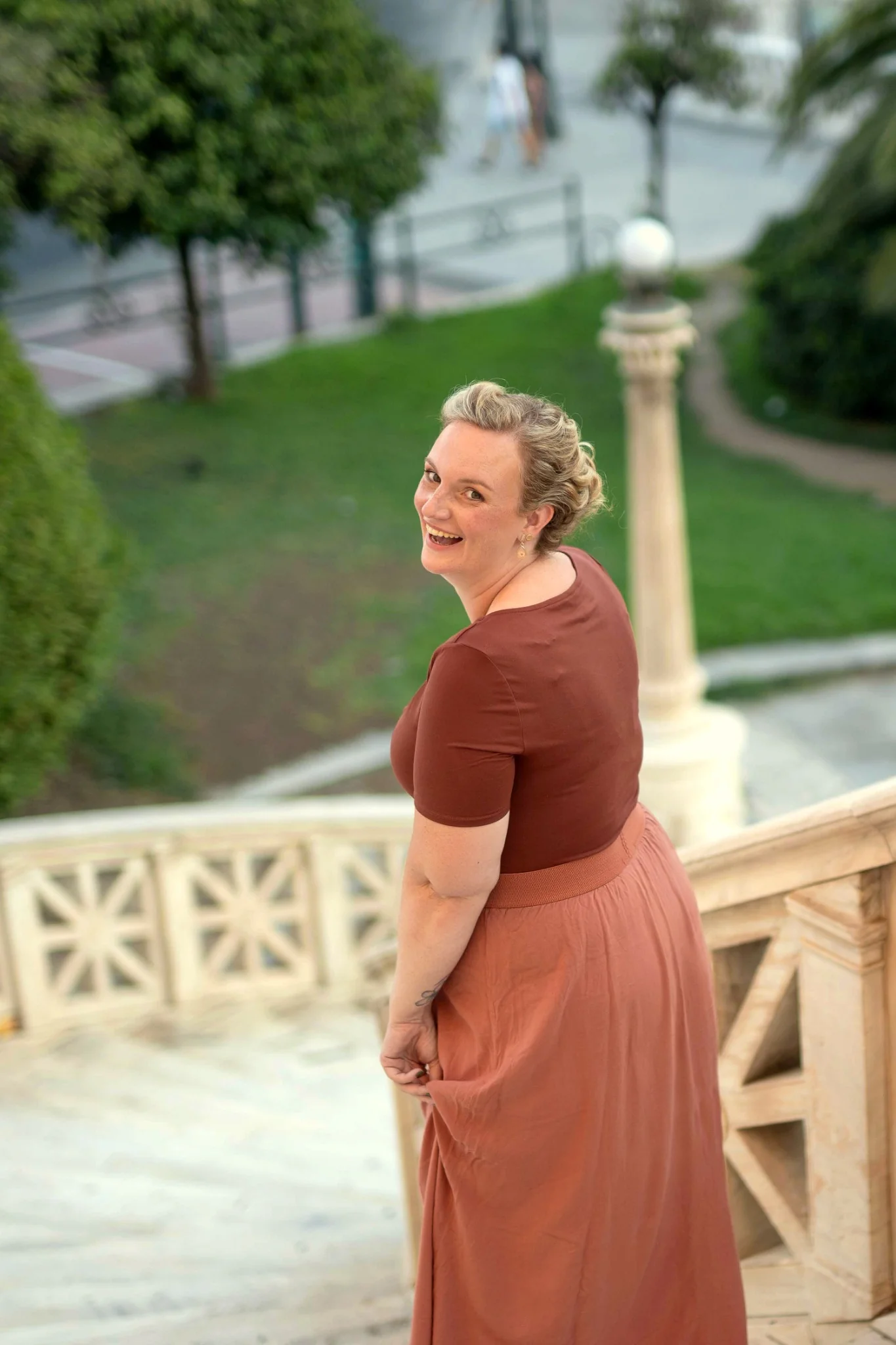 Melina looking back and smiling on a stone terrace above a green courtyard