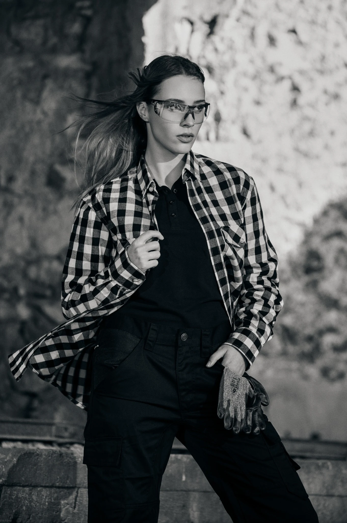 Black-and-white portrait of a model in a checked work shirt and protective glasses