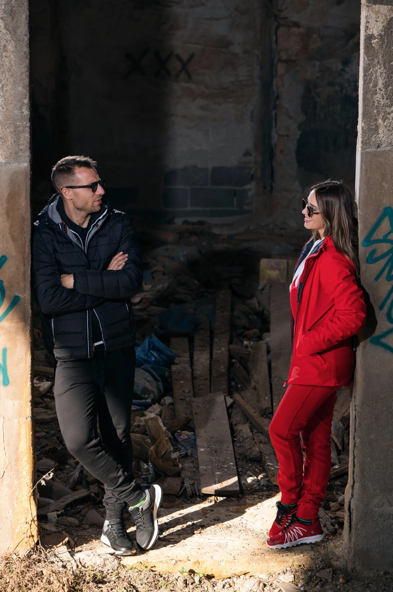 Two models facing each other in a weathered industrial doorway, wearing red and black outerwear