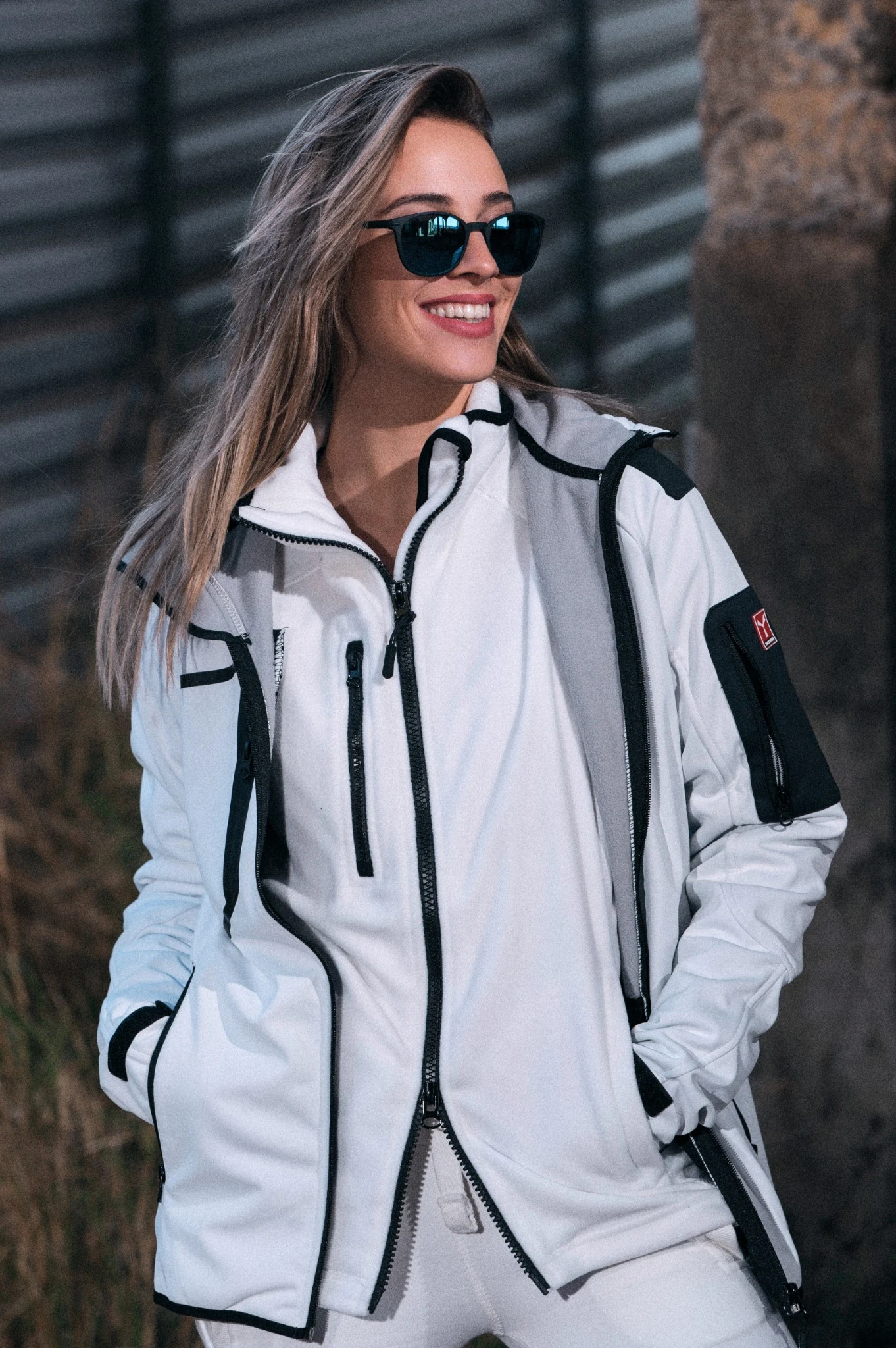 Smiling model wearing sunglasses and a white work jacket with black trim