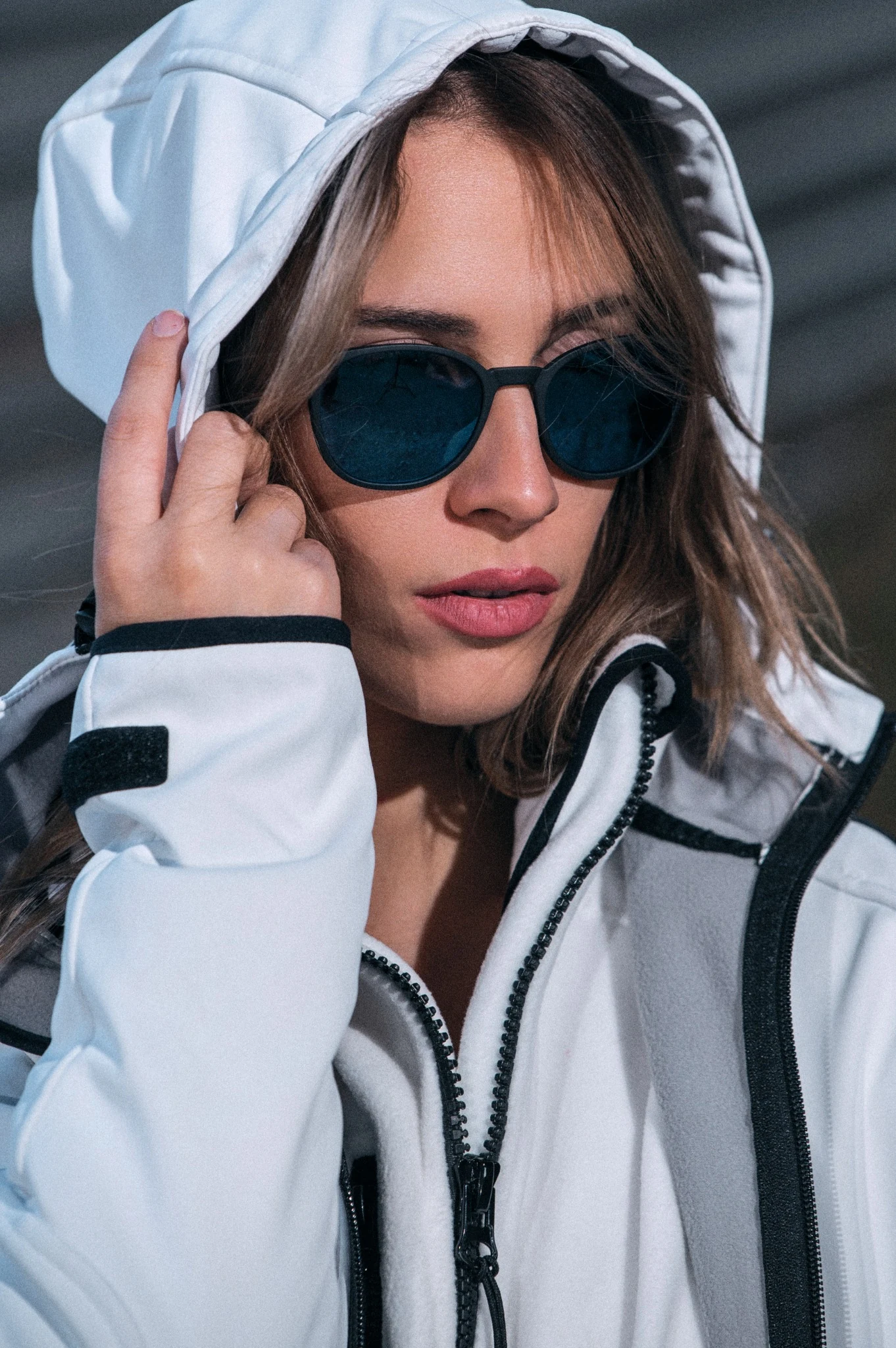 Close portrait of a model in a white hooded jacket and dark sunglasses