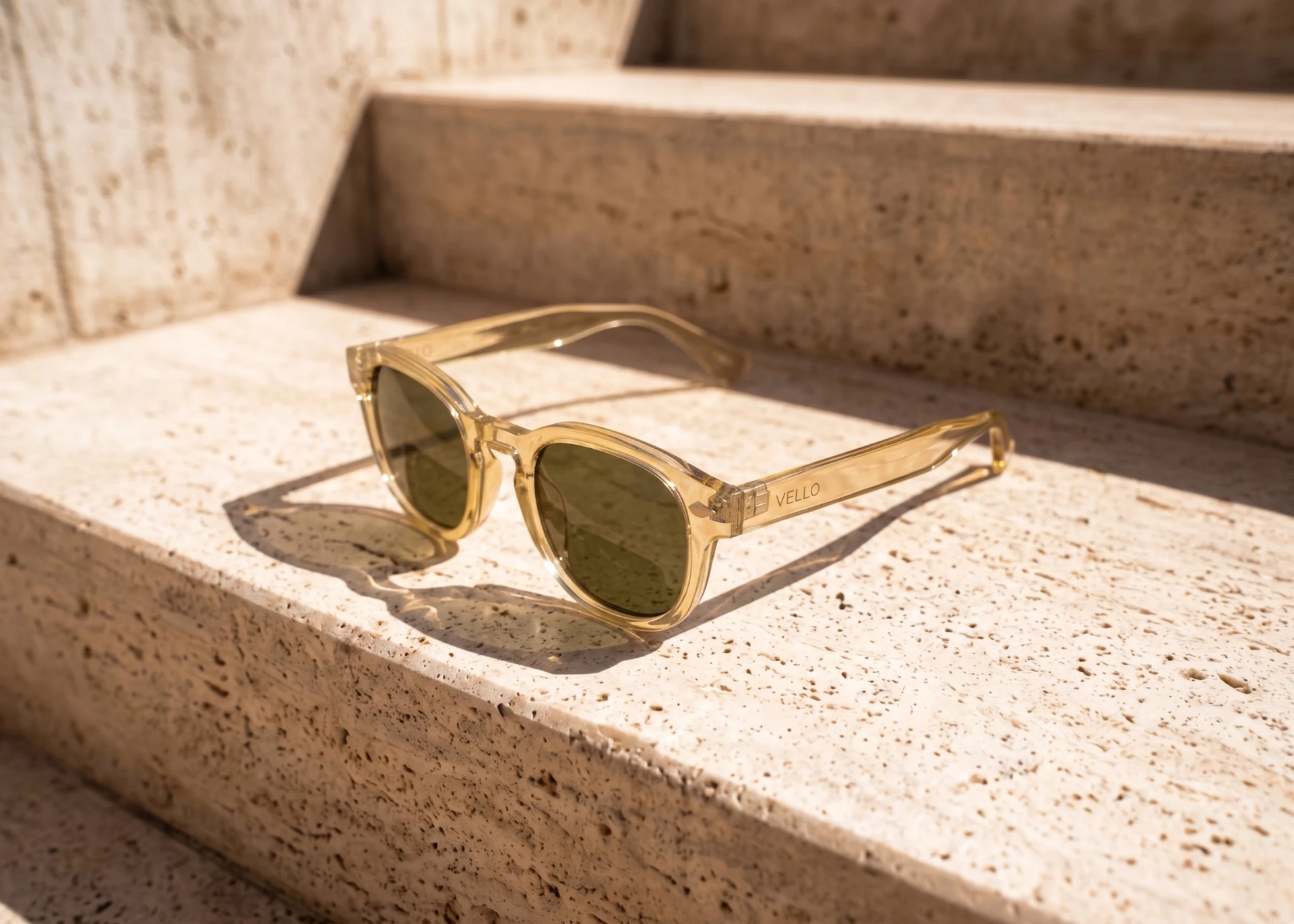 Translucent amber Vello sunglasses with green lenses on warm stone steps